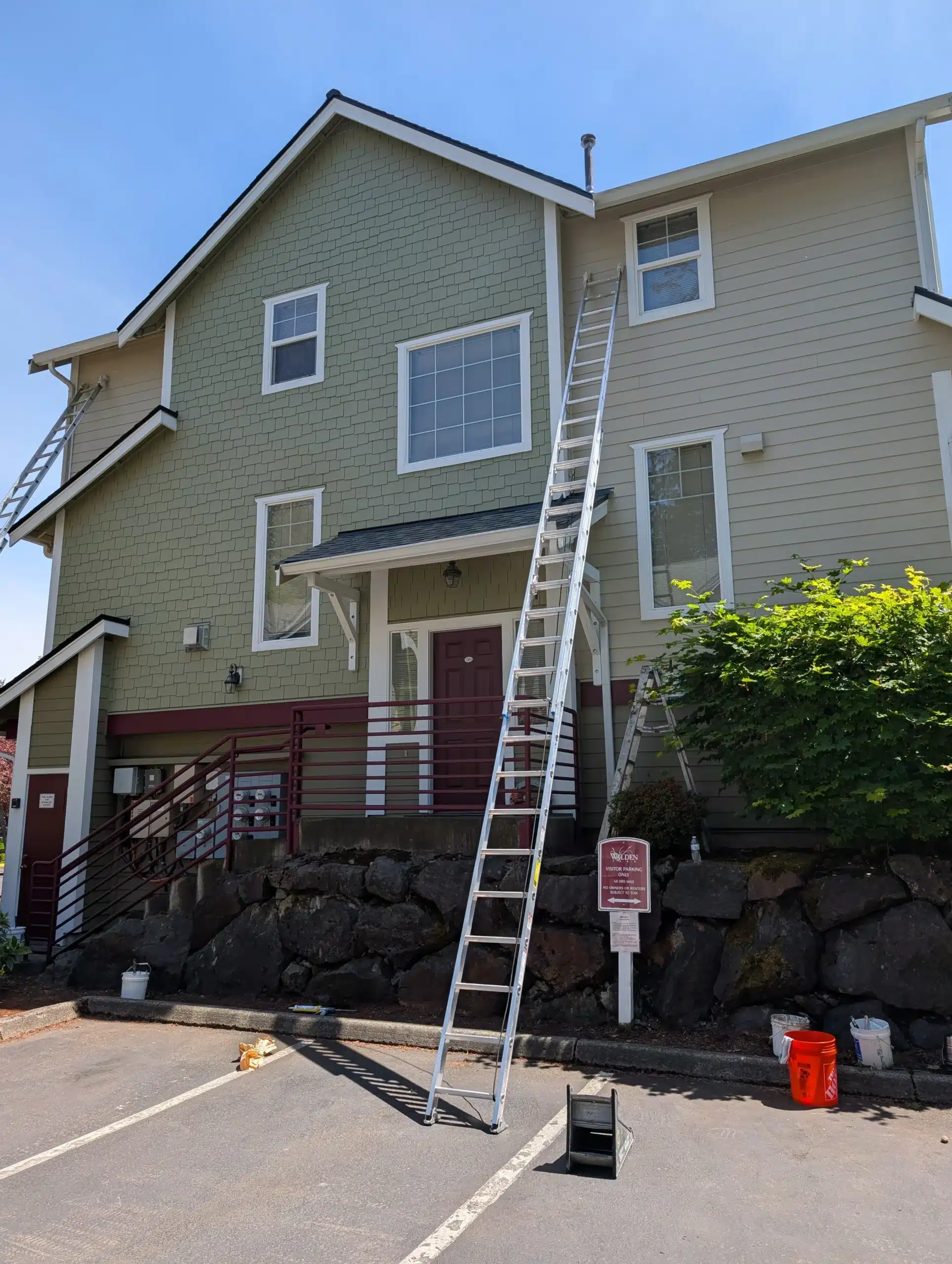 Commercial Exterior Painting Project on Multi-Story Building Professional painters using extension ladders during exterior painting of a multi-story commercial residential building with green and beige siding.