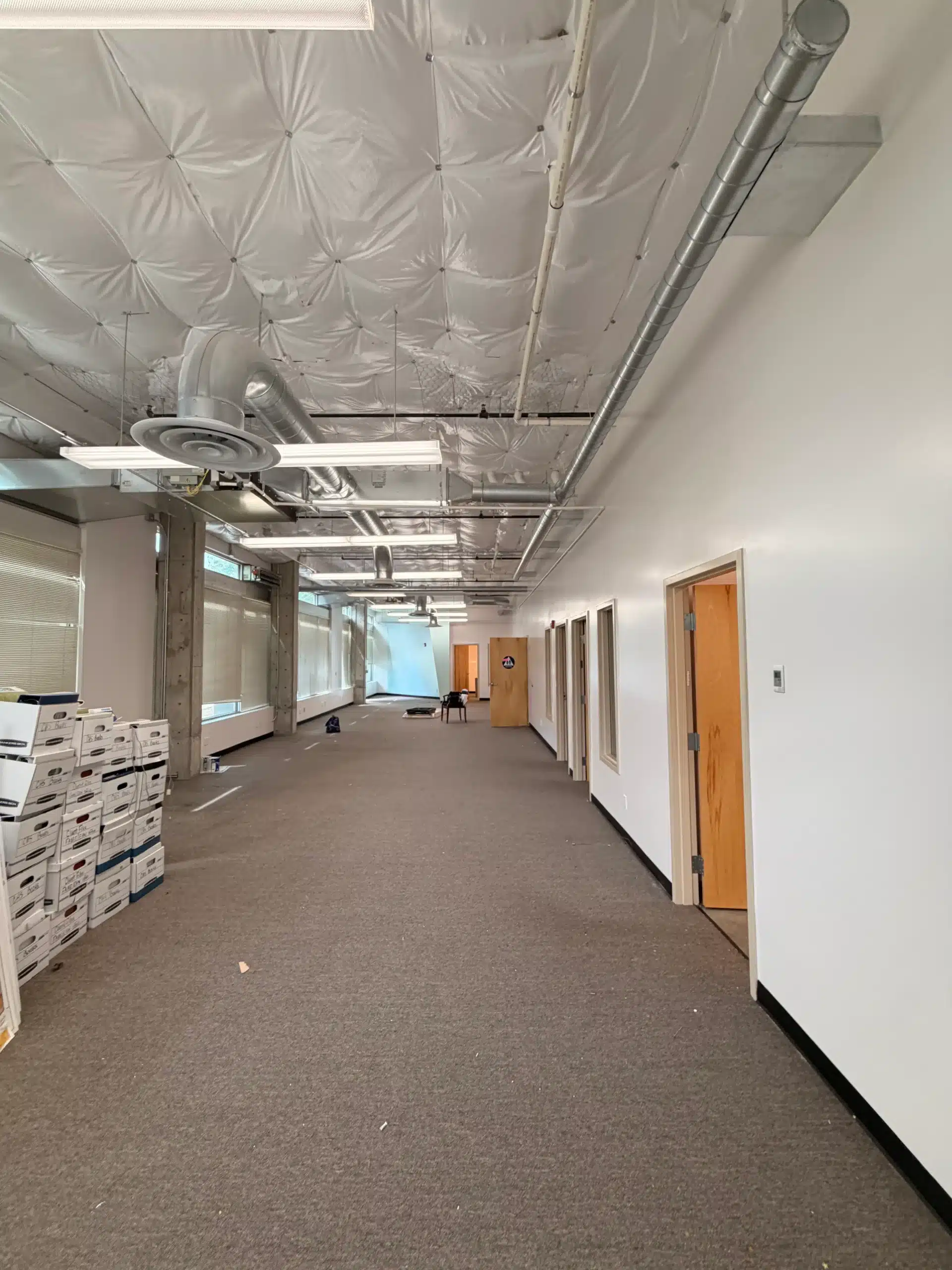 Commercial office interior painting services for large spaces Long empty commercial office hallway with white walls, exposed ceiling, and carpeted floor.