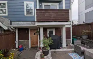 Lower exterior of a residential building featuring blue siding, brown shingles, and a wooden fence.