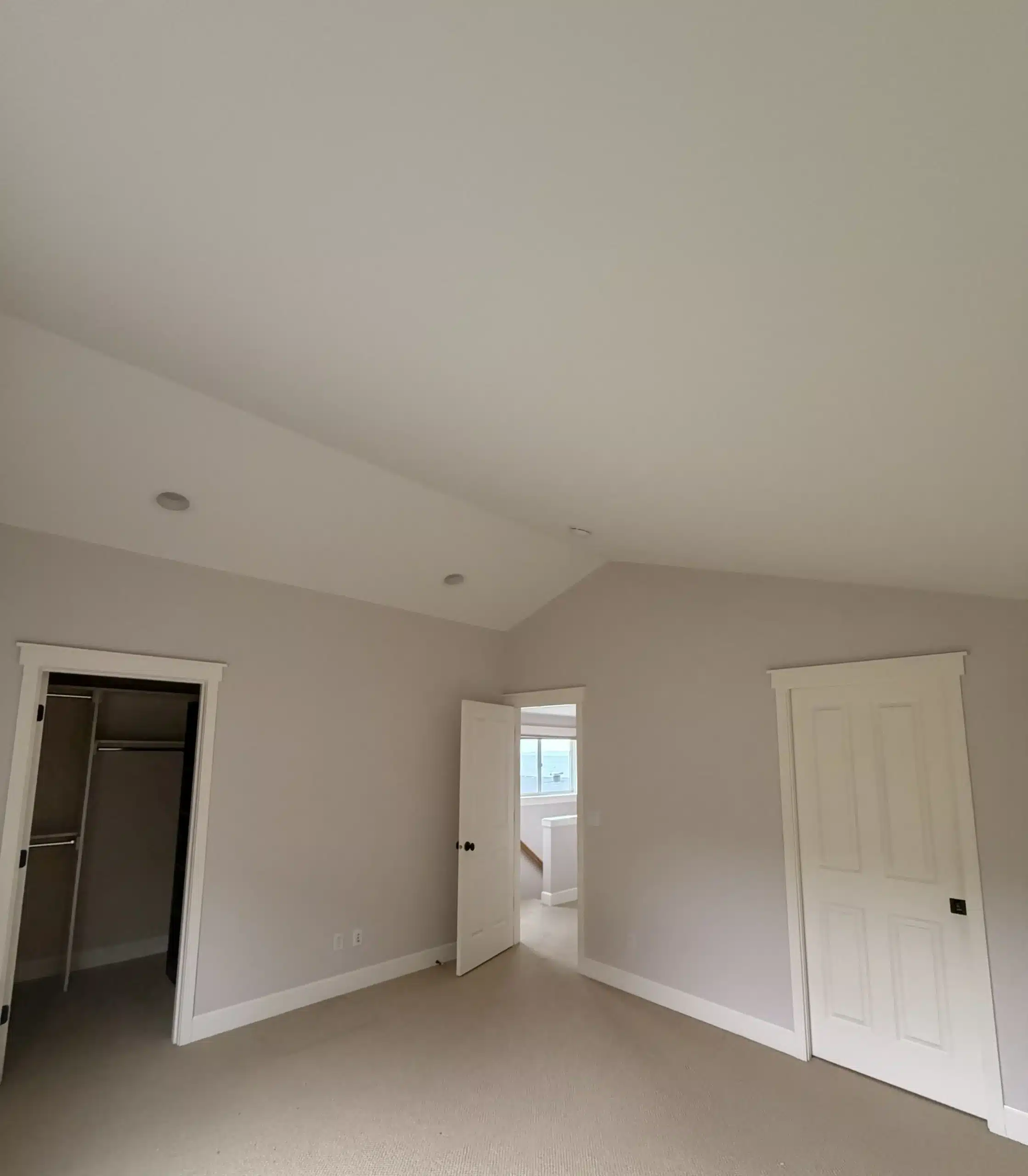 Light Gray Bedroom Interior Painting Service Spacious bedroom with newly painted light gray walls, white trim, and carpet, showcasing professional interior painting.