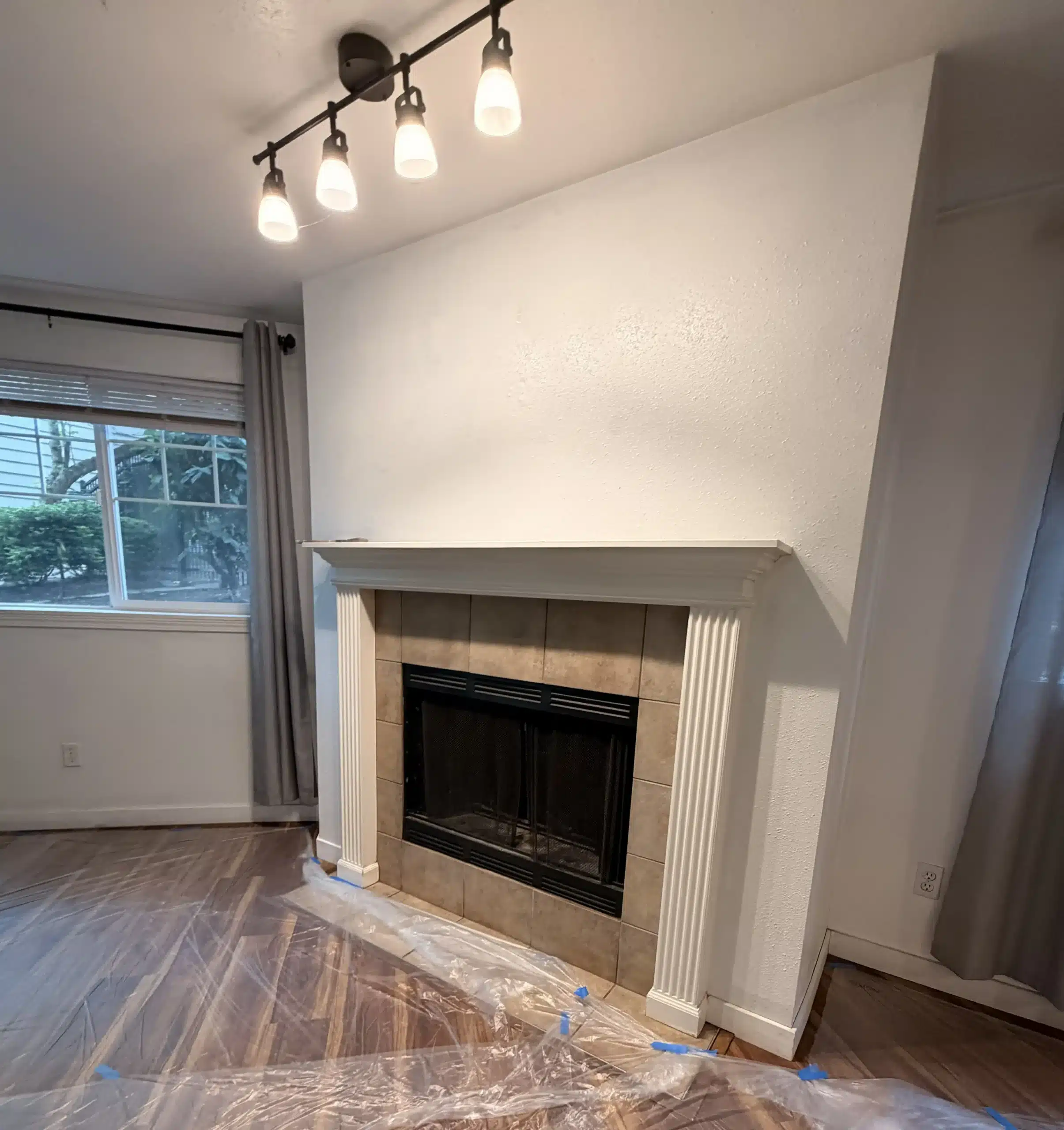 Professional Fireplace Wall Painting and Surface Protection Fireplace wall with fresh white paint, track lighting, and protected wood floors during professional interior painting.