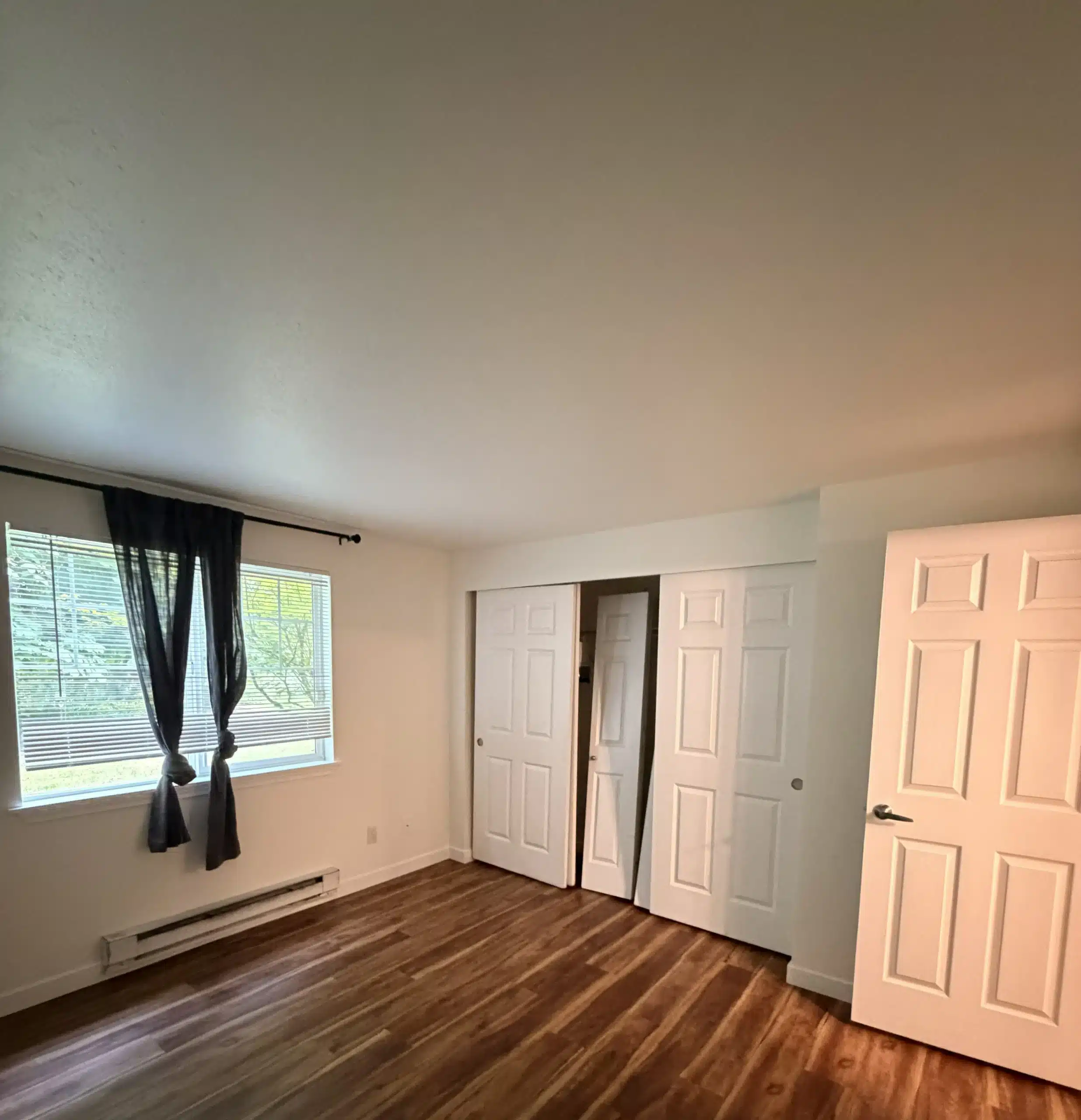 Freshly Painted Bedroom with White Walls and Wood Floors Empty bedroom with new white paint, wood floors, and closet doors, ready for residential interior painting.